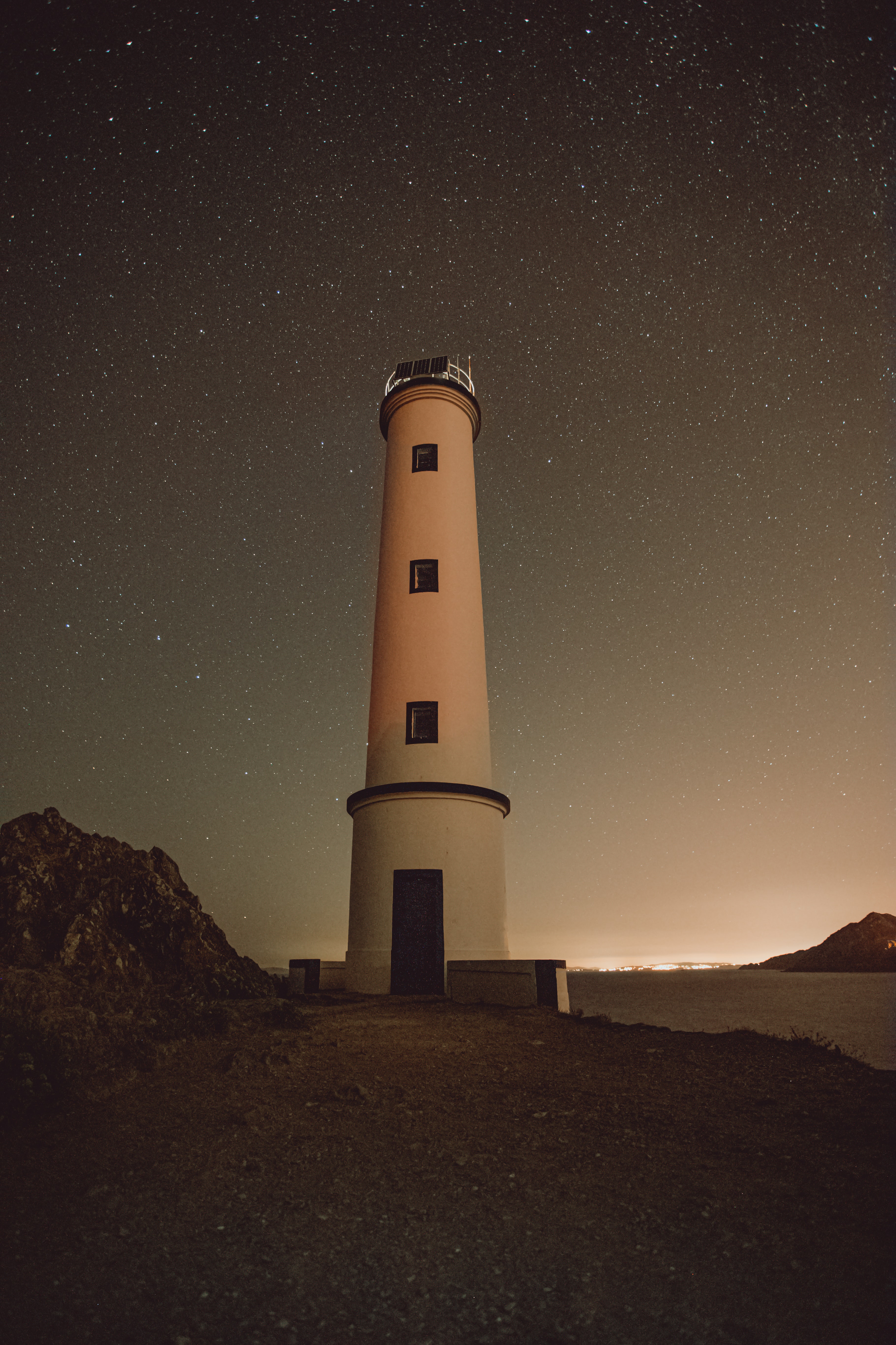 Download mobile wallpaper Stars, Rocks, Building, Starry Sky, Lighthouse, Night, Nature for free.